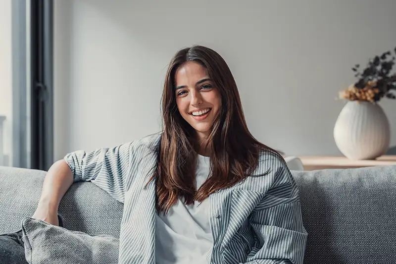 Happy young woman smiling while seated on a couch, representing a proud and empowered surrogate candidate with LifeBridge Surrogacy