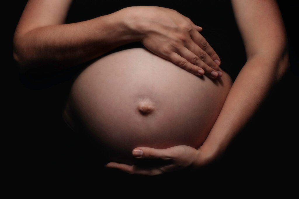 Pregnant woman cradling unborn child. Low key image.